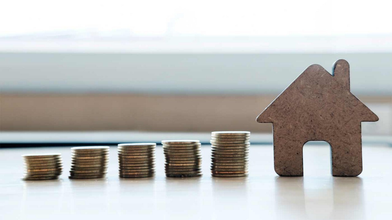 4 stacks of coins in varying heights and a cut out house to indicate saving for a house.