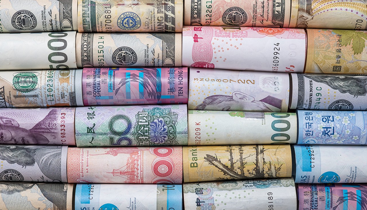 Various foreign currencies are rolled and lined up in rows.