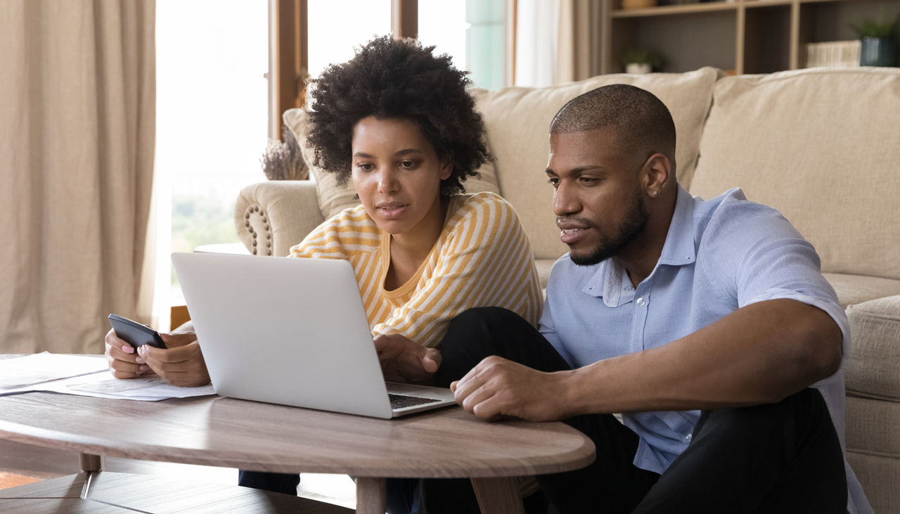 Young Black couple sitting in living room reviewing a laptop and paperwork