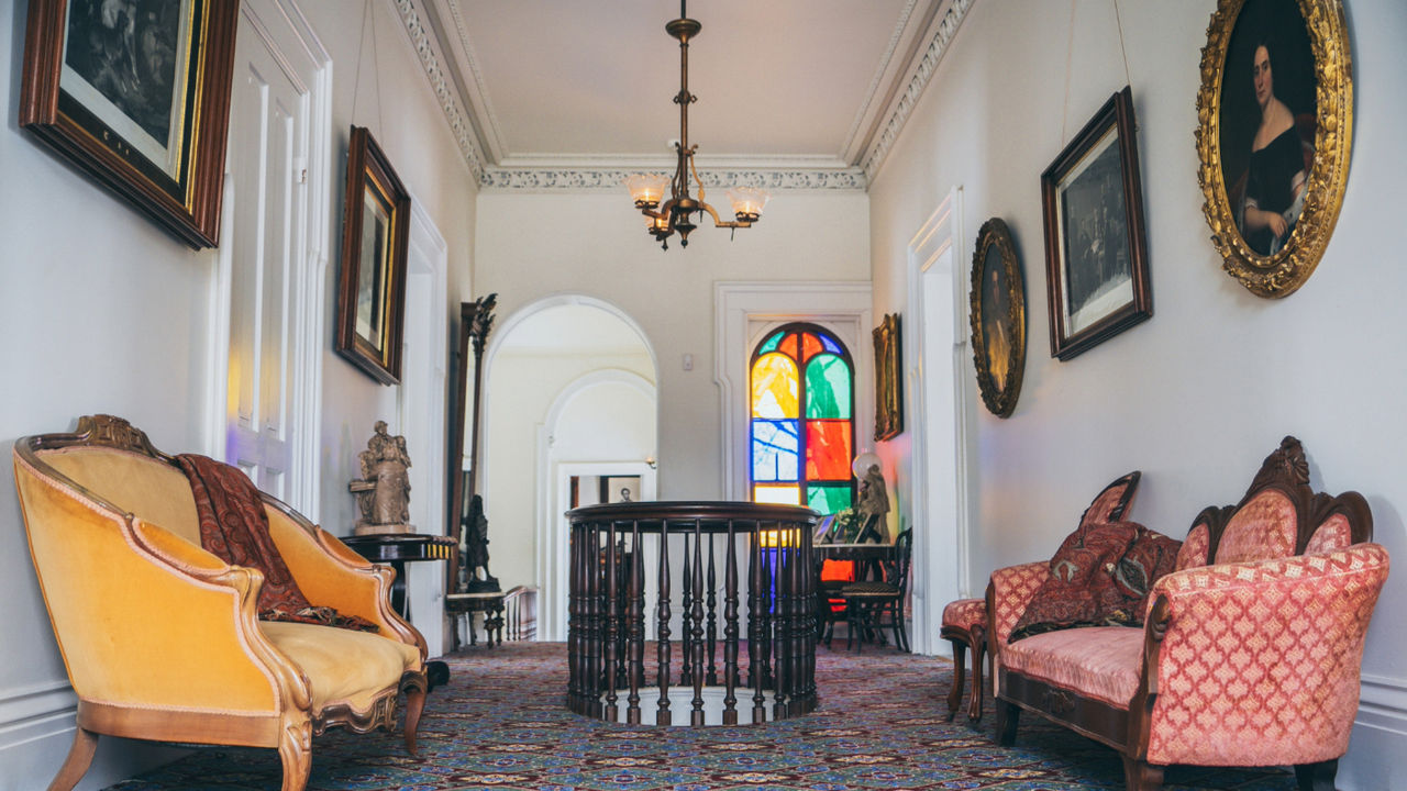 Interior hallway of the Lincoln-Tallman House featuring furniture on the right and left side of the hallway, photos on the walls, period artwork, and colorful stained-glass window.